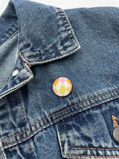 A fabric-covered lapel pin with a pastel checkered print. The pin is worn on a denim jacket.