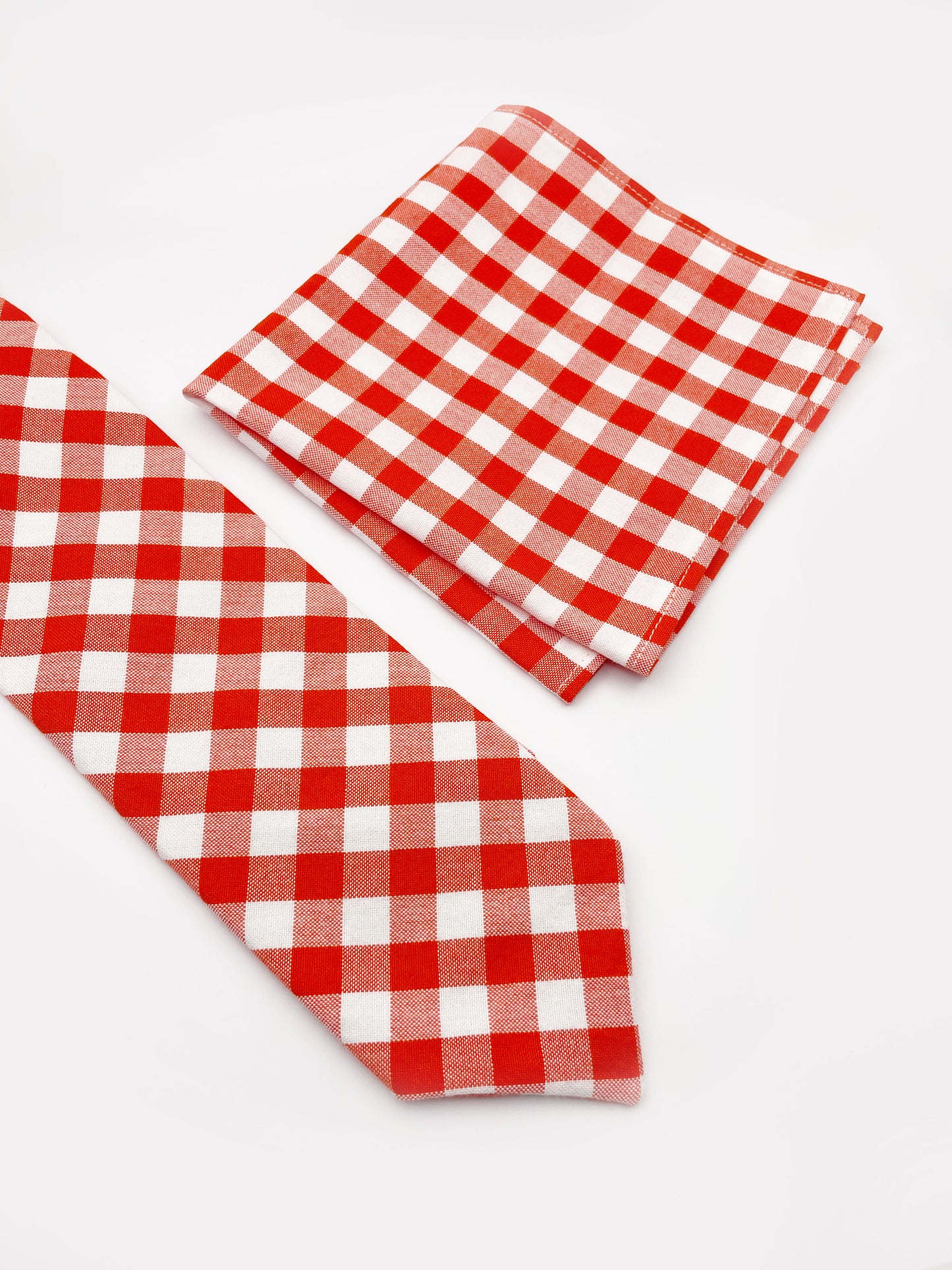 A cotton necktie with a vibrant red gingham plaid print next to a matching pocket square.