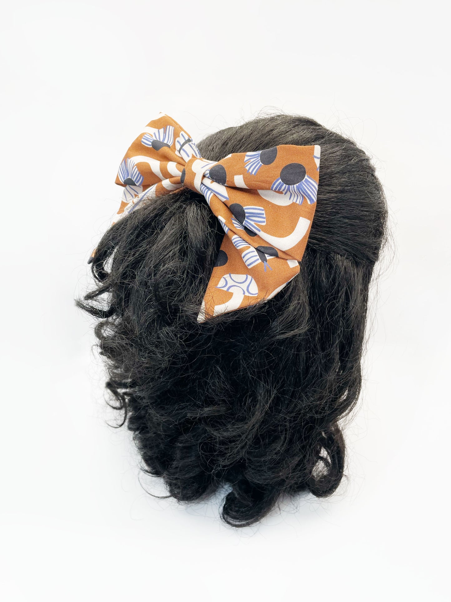 A large handmade hair bow with an abstract floral and leaf print in cream, black, and soft blue. The bow is modeled on a mannequin head.