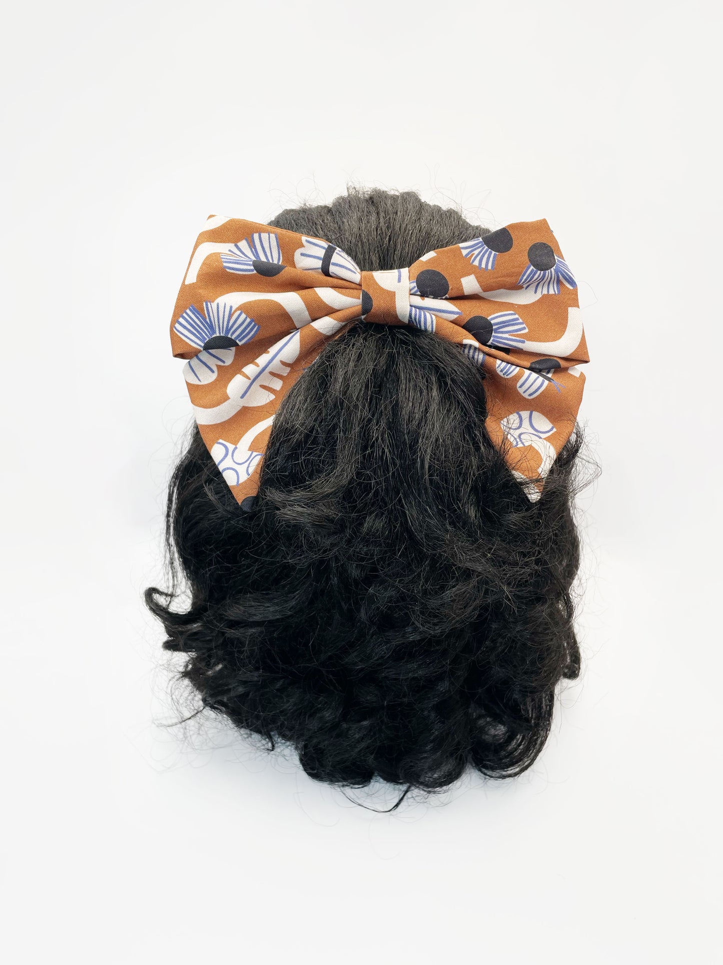 A large handmade hair bow with an abstract floral and leaf print in cream, black, and soft blue. The bow is modeled on a mannequin head.