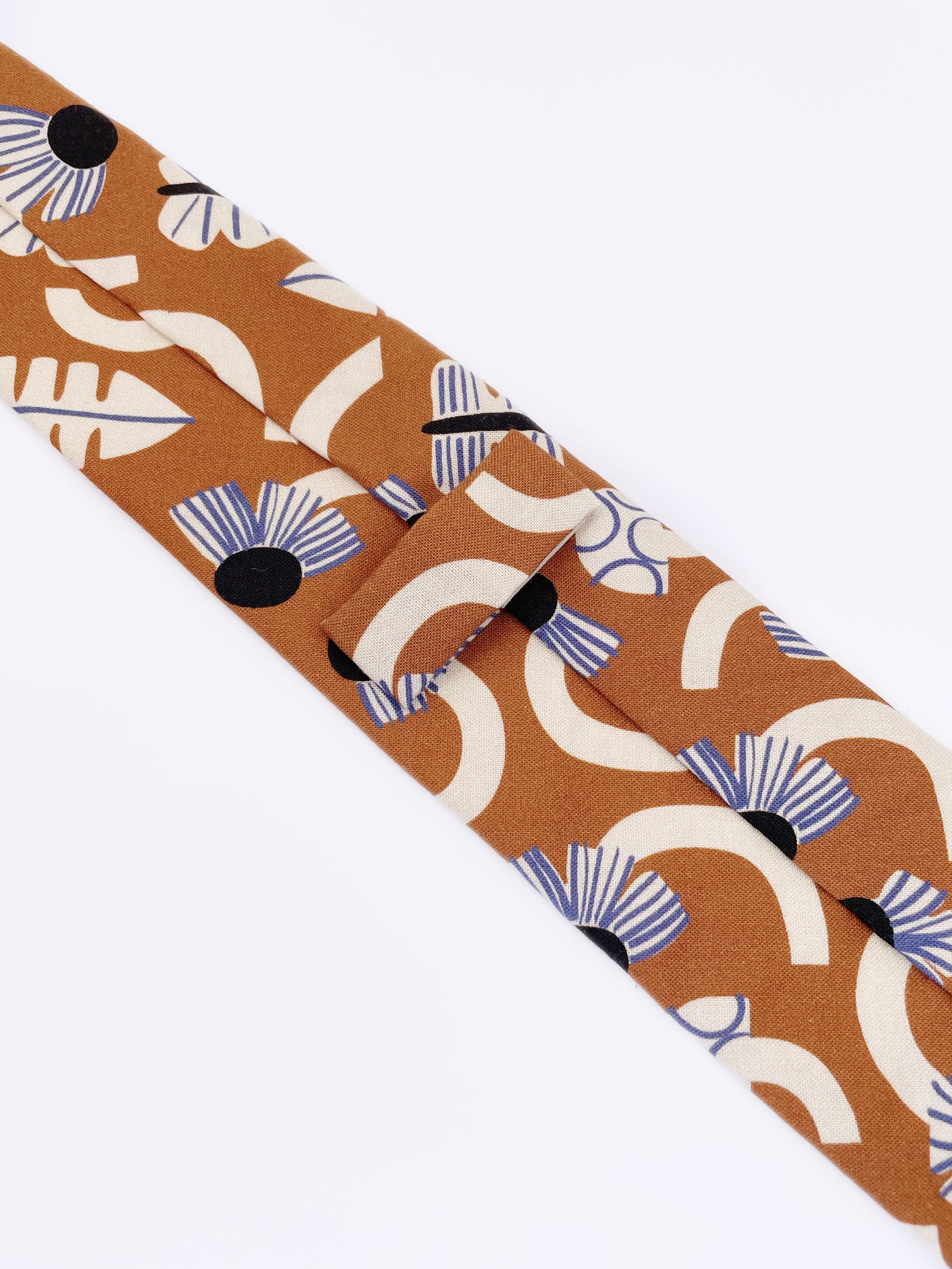 A necktie with an abstract print featuring flowers, leaves, mushrooms, and butterflies on a rich terracotta background. The color palette also consists of cream, black, and blue.