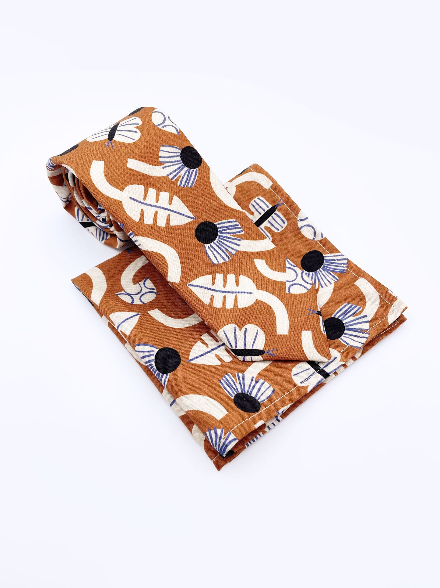 A necktie with an abstract print featuring flowers, leaves, mushrooms, and butterflies on a rich terracotta background. The necktie is shown with a matching pocket square.