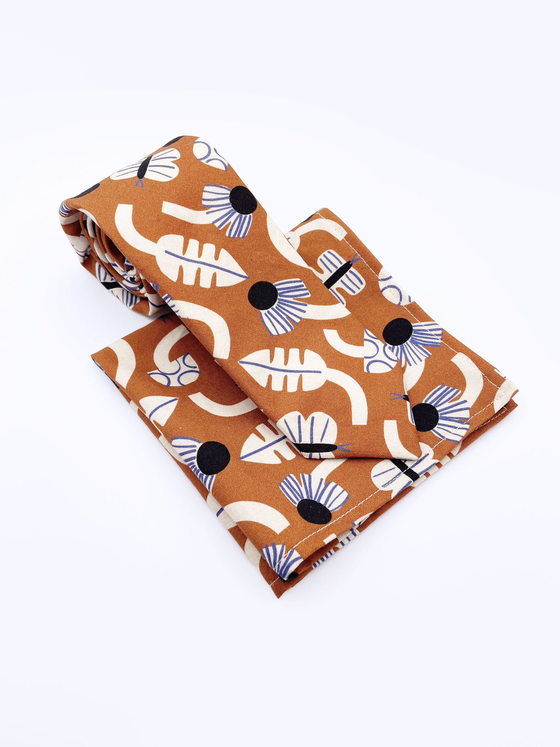 A necktie with an abstract print featuring flowers, leaves, mushrooms, and butterflies on a rich terracotta background. The necktie is shown with a matching pocket square.