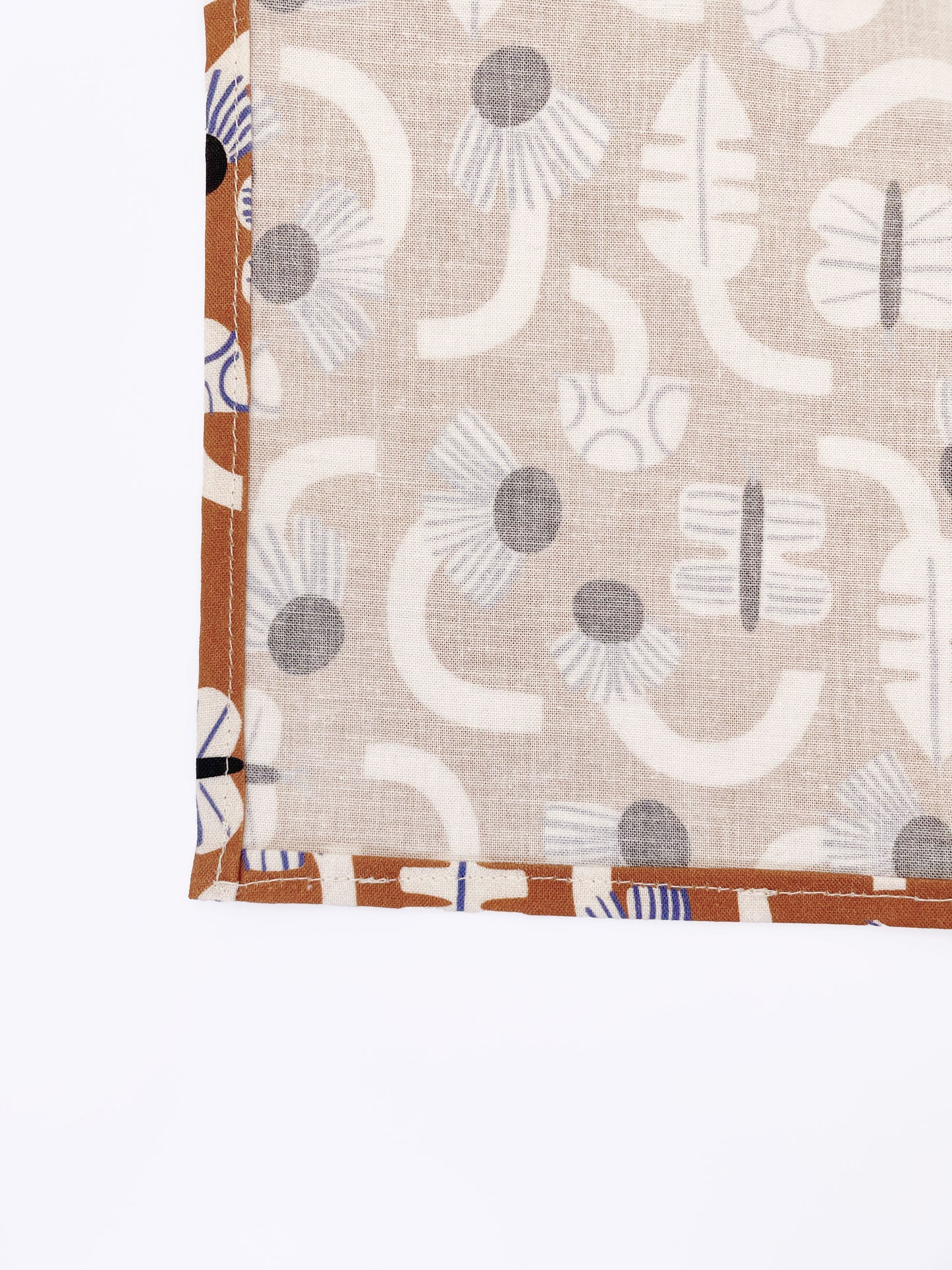 A pocket square with an abstract print featuring flowers, leaves, mushrooms, and butterflies on a rich terracotta background. The color palette also consists of cream, black, and blue.