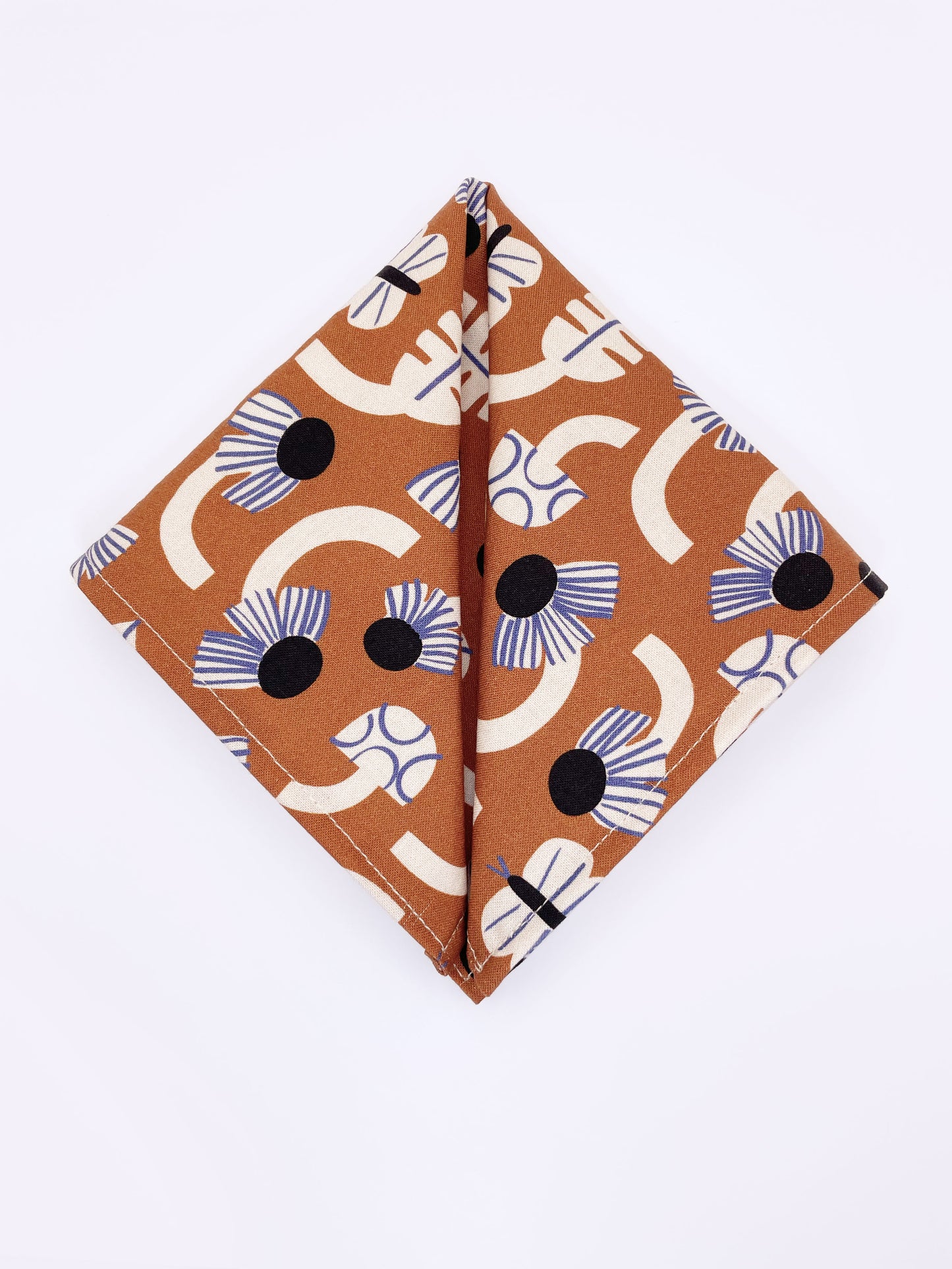 A pocket square with an abstract print featuring flowers, leaves, mushrooms, and butterflies on a rich terracotta background. The color palette also consists of cream, black, and blue.