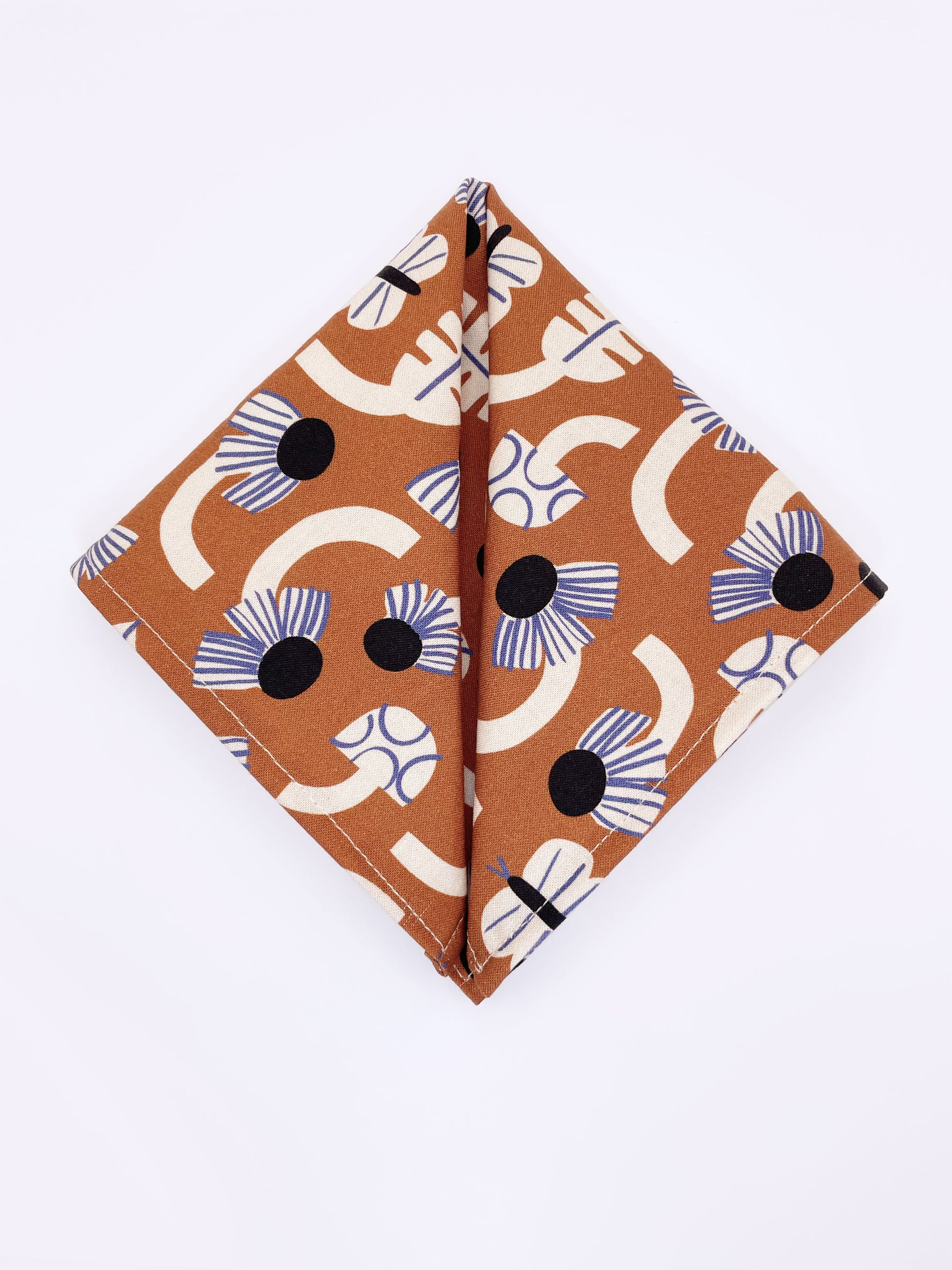 A pocket square with an abstract print featuring flowers, leaves, mushrooms, and butterflies on a rich terracotta background. The color palette also consists of cream, black, and blue.