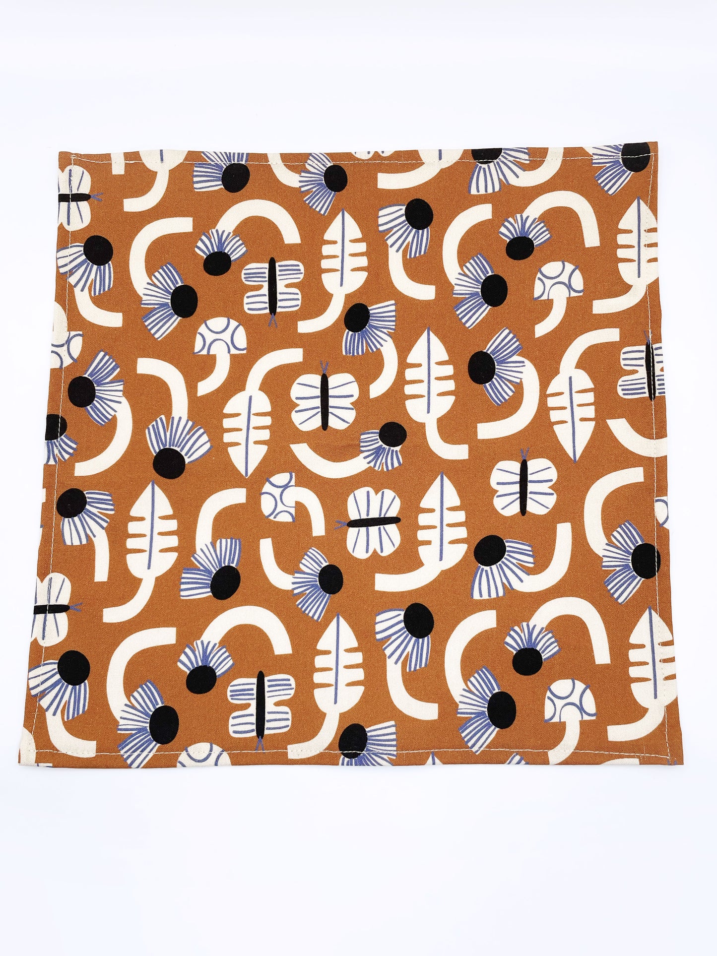 A pocket square with an abstract print featuring flowers, leaves, mushrooms, and butterflies on a rich terracotta background. The color palette also consists of cream, black, and blue.