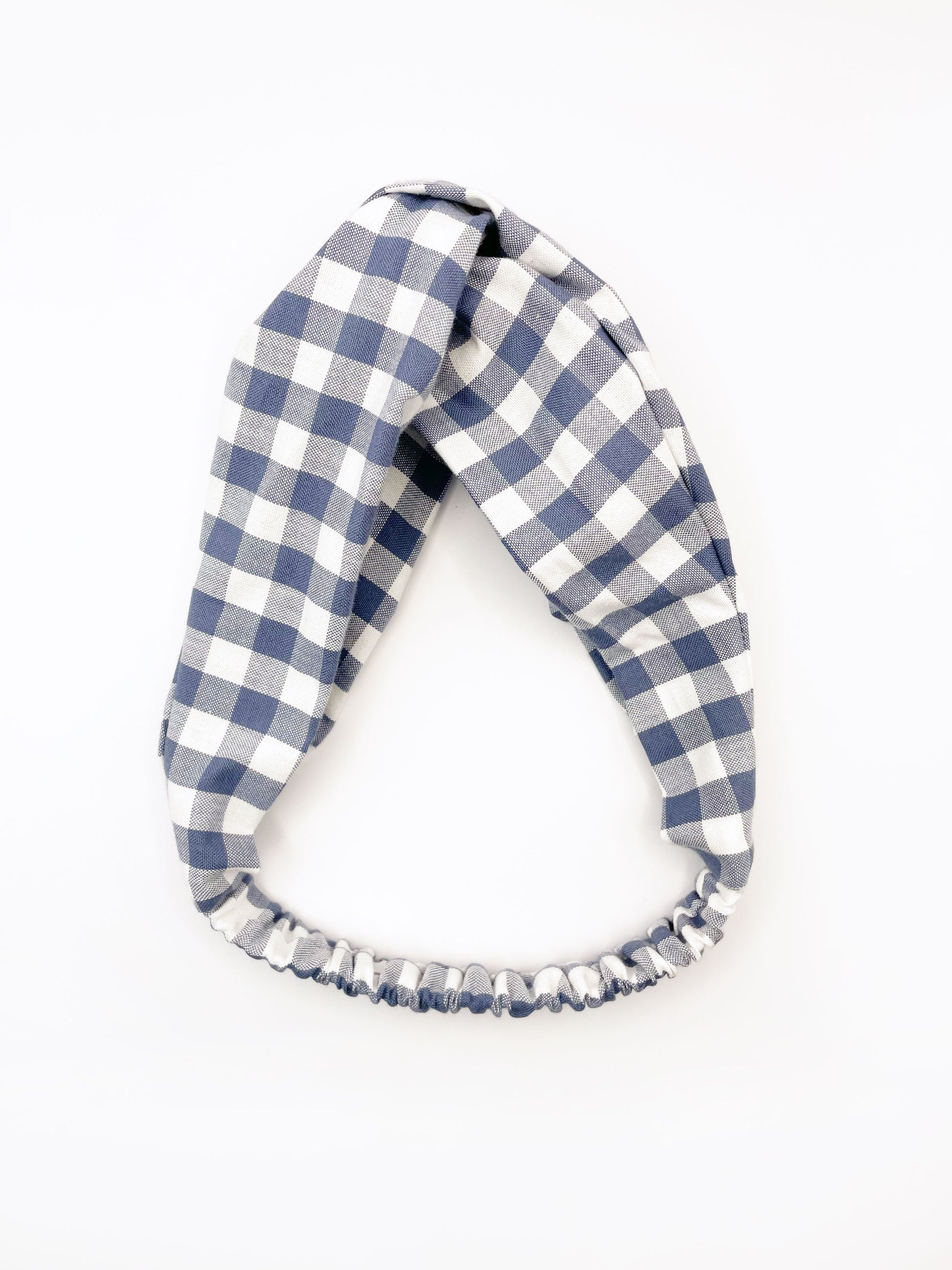 A cotton twist headband with a classic slate blue gingham plaid print. The headband has an elastic band in the back to prevent slipping.