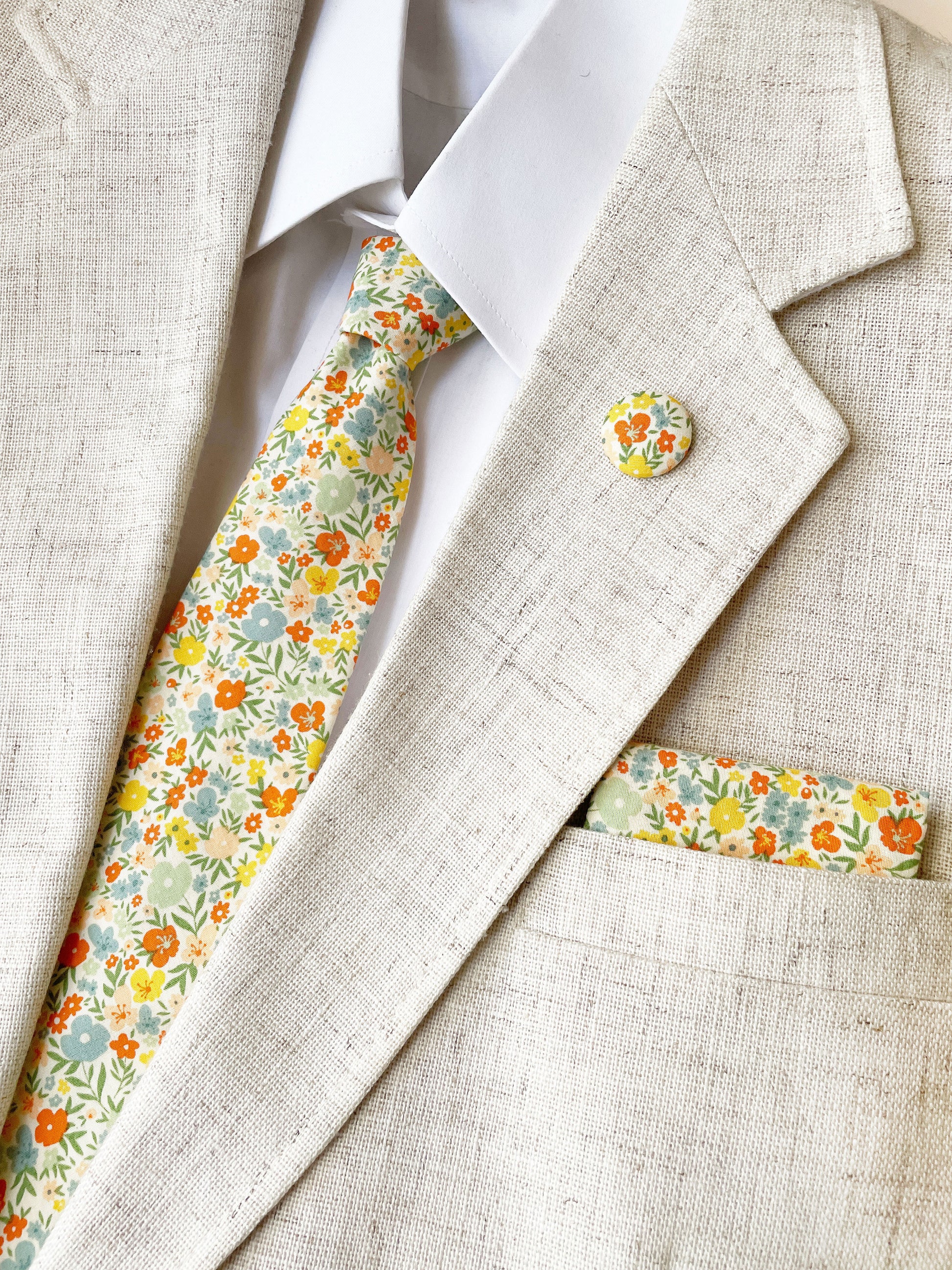 A handmade pocket square featuring colorful flowers worn with a matching necktie and lapel pin.