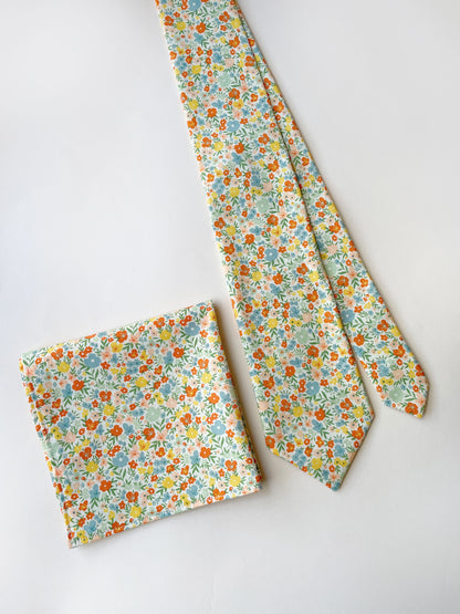 A handmade pocket square featuring colorful flowers next to a matching necktie.