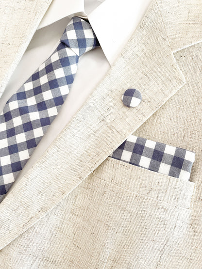 A handmade slate blue gingham plaid pocket square with a matching necktie and lapel pin.