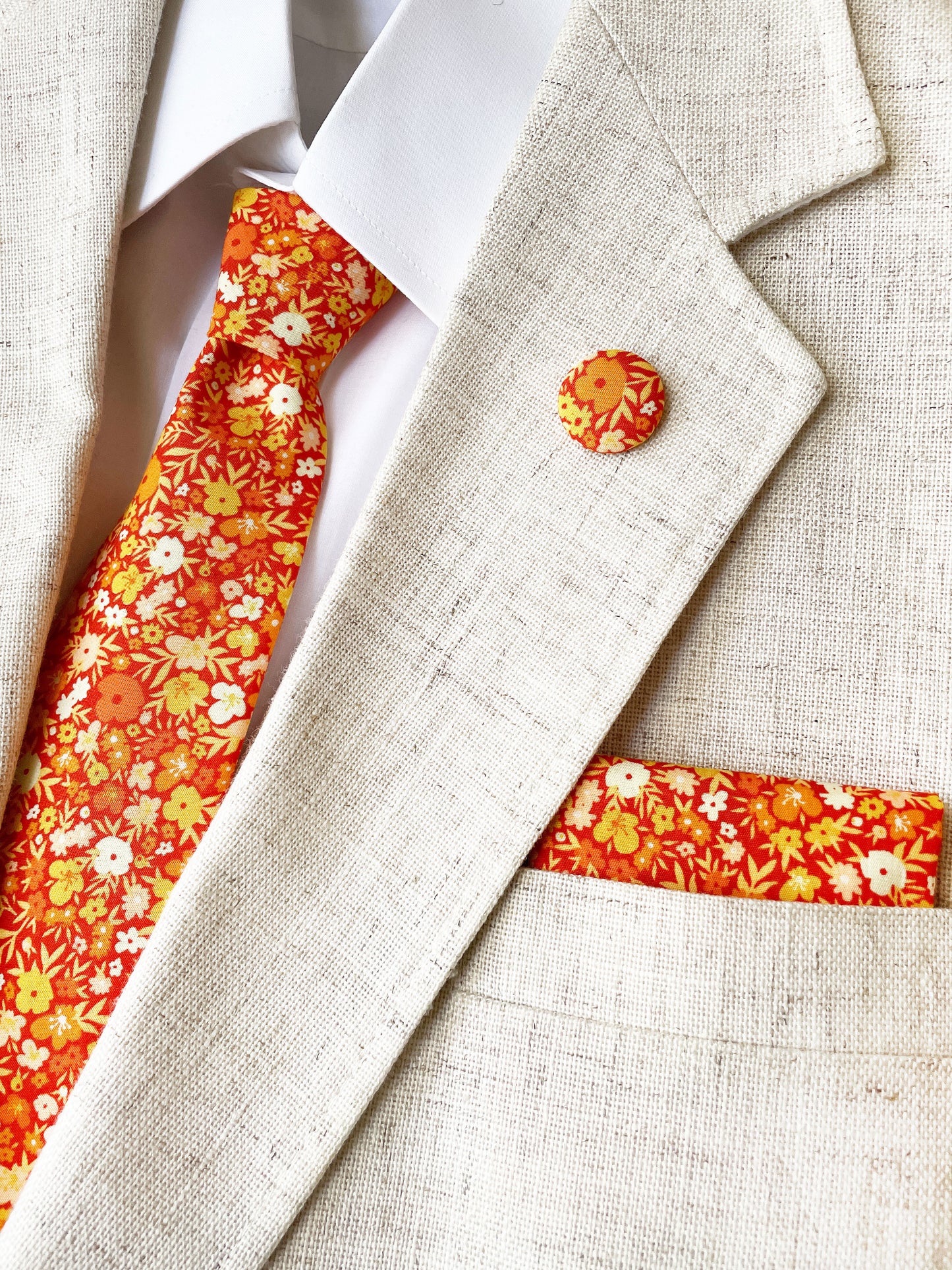 A handmade pocket square featuring vibrant orange and yellow flowers worn with a matching necktie and lapel pin.