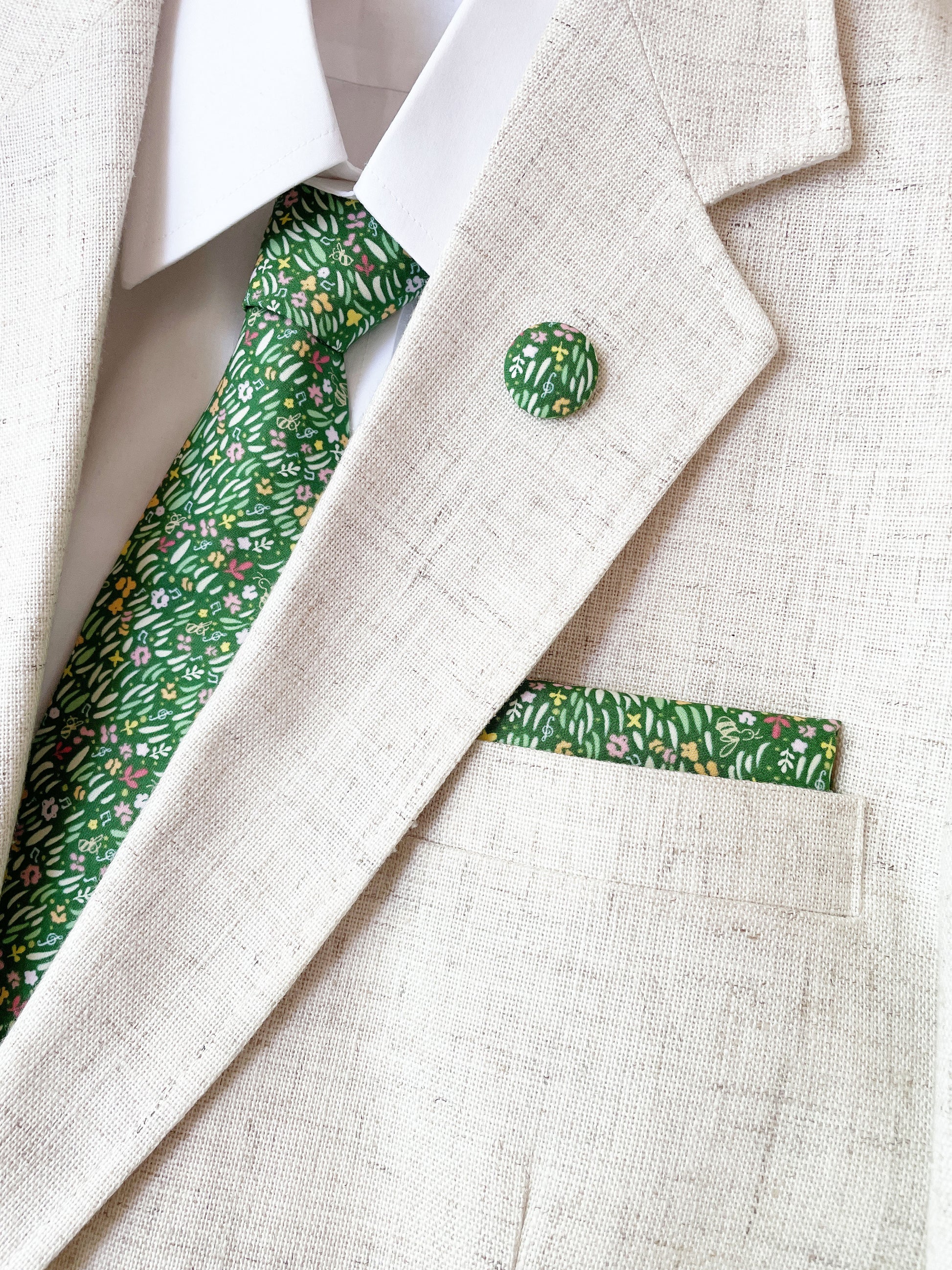 A handmade green floral pocket square with a grass print worn with a matching necktie and lapel pin.