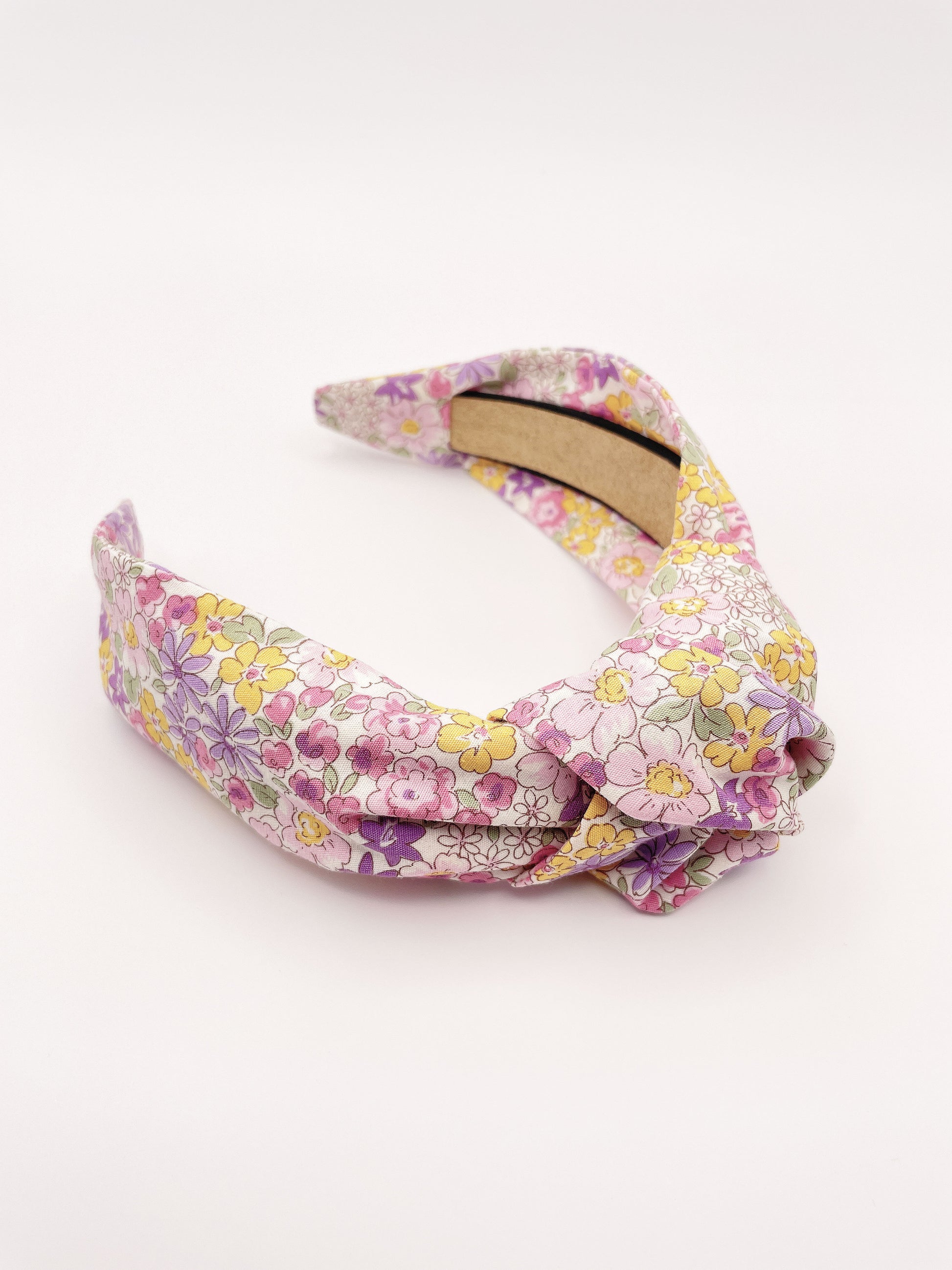 Handmade knotted headband with purple flowers against an off white background.