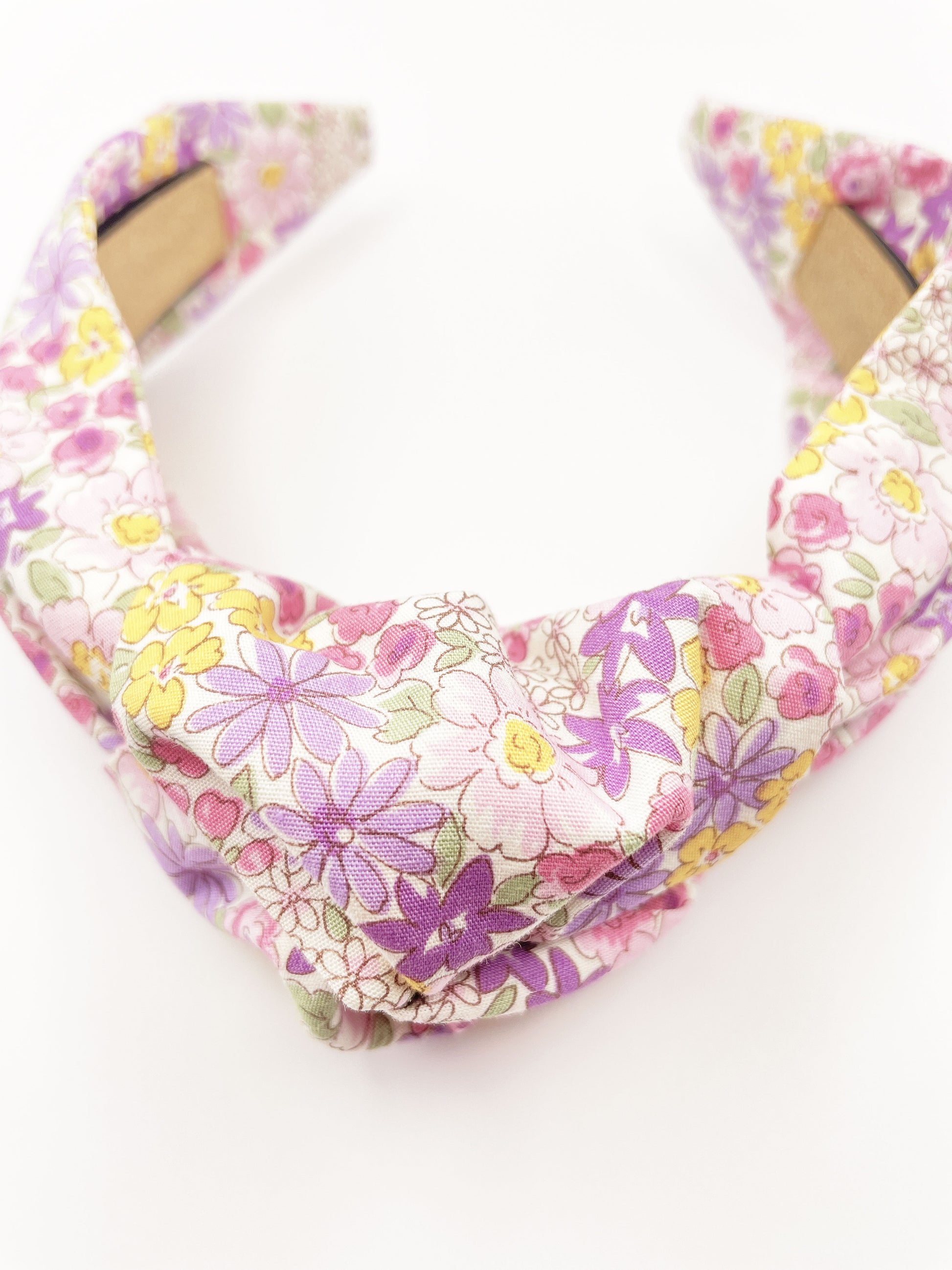 Handmade knotted headband with purple flowers against an off white background.