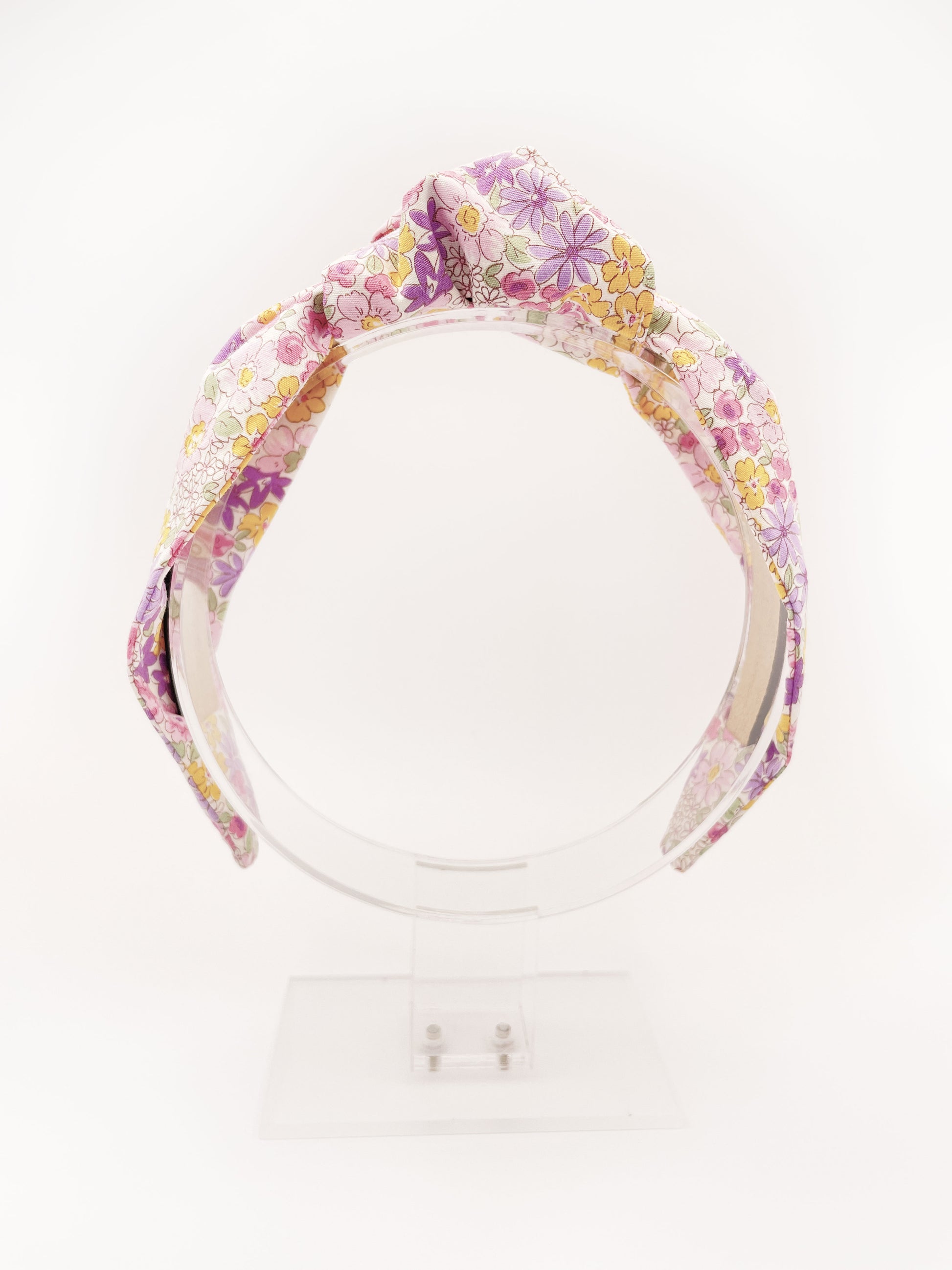 Handmade knotted headband with purple flowers against an off white background.