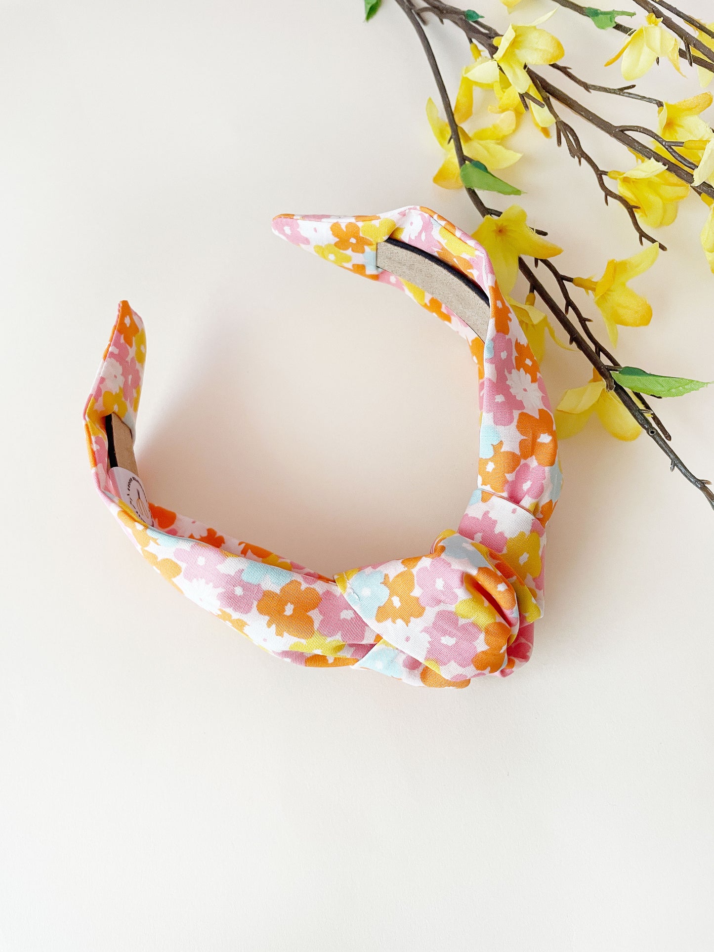 A handmade colorful floral knotted headband next to yellow flowers.