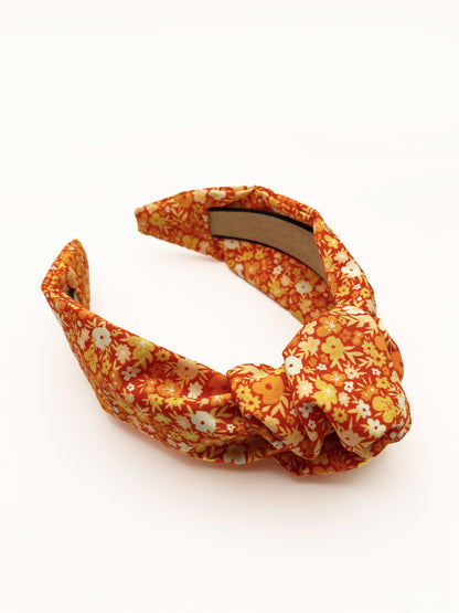 An orange boho knotted headband with a vibrant floral print.