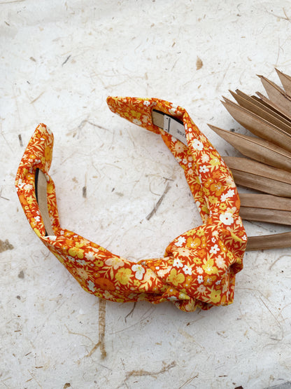 An orange boho knotted headband with a vibrant floral print.