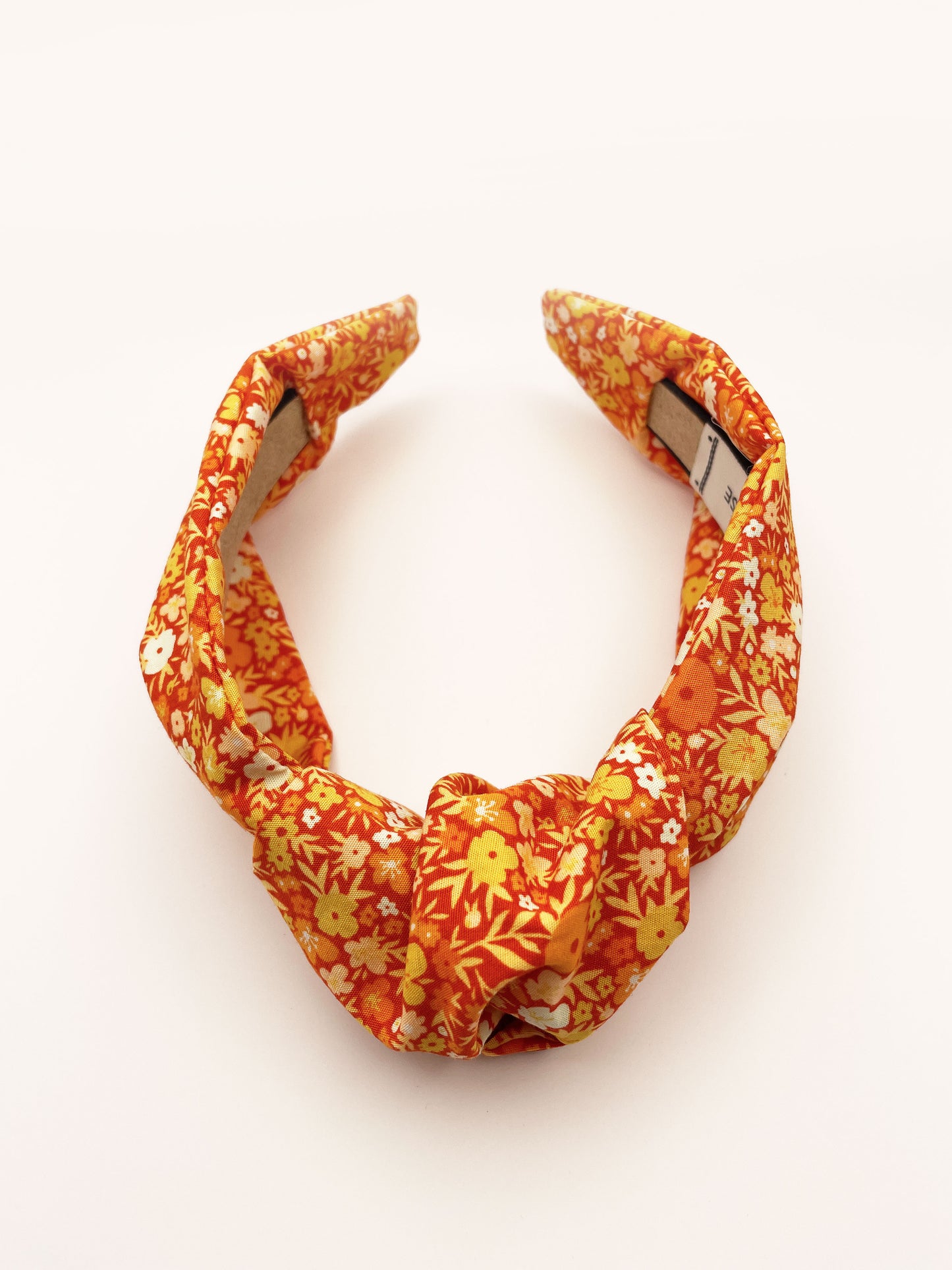 An orange boho knotted headband with a vibrant floral print.