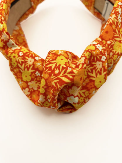 An orange boho knotted headband with a vibrant floral print.