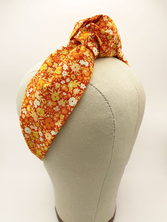 An orange boho knotted headband with a vibrant floral print.