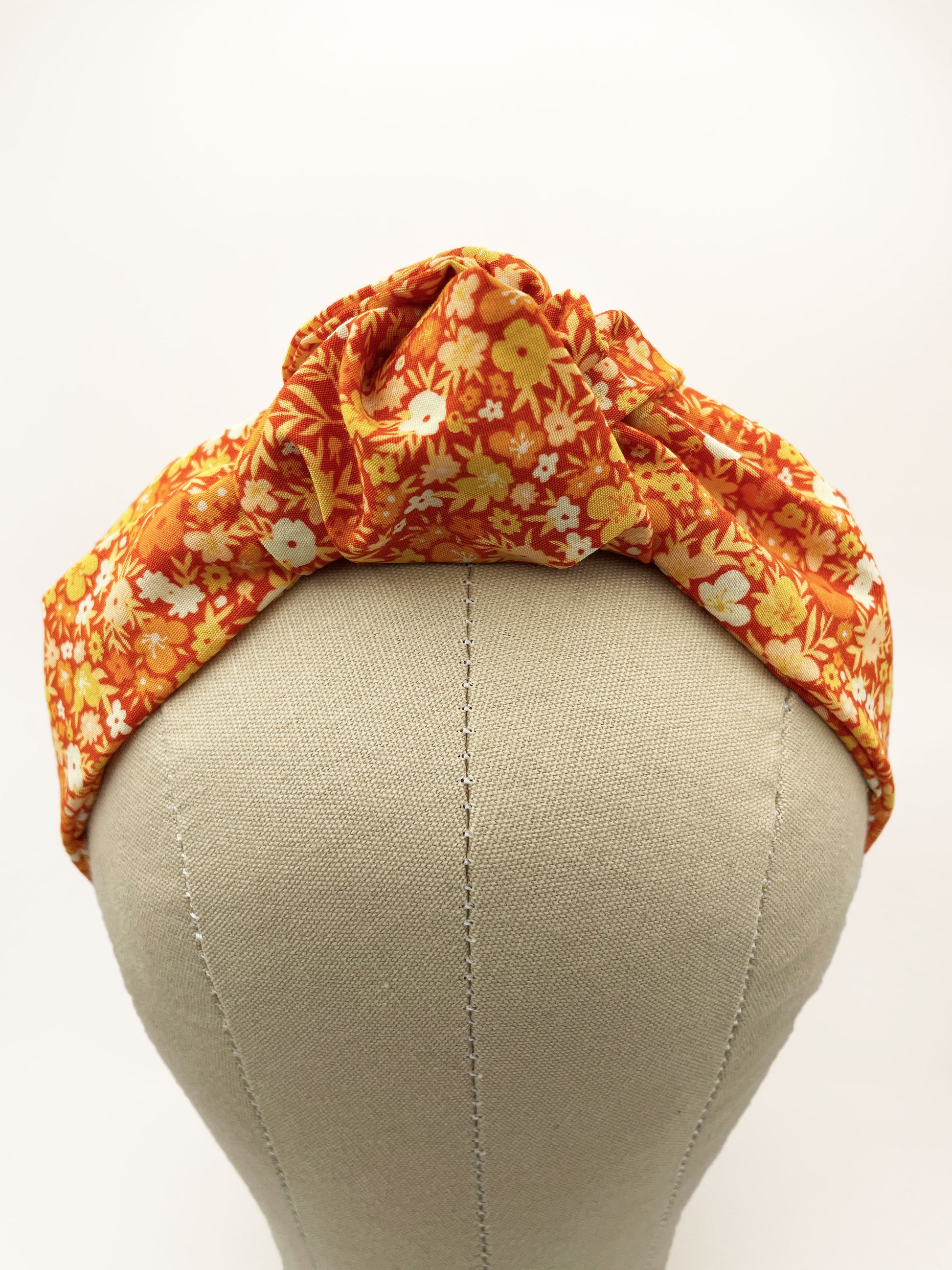 An orange boho knotted headband with a vibrant floral print.