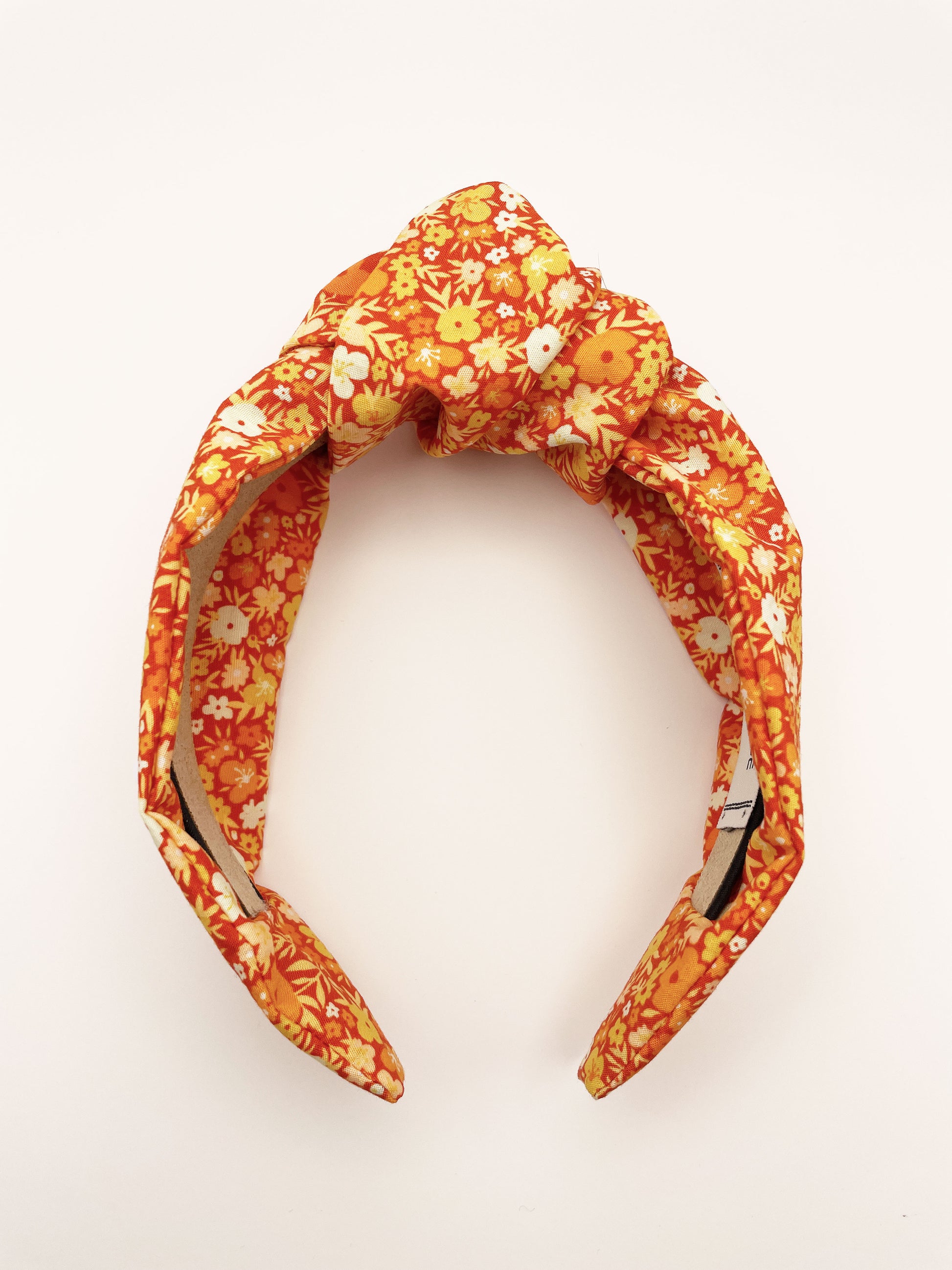 An orange boho knotted headband with a vibrant floral print.