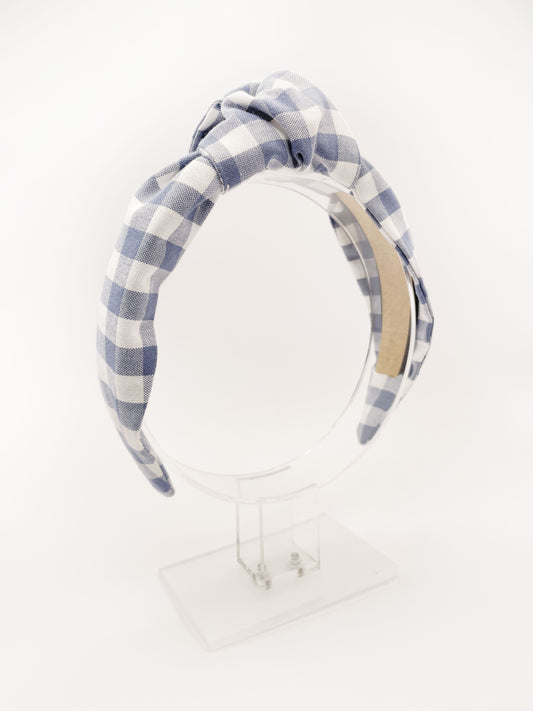 A handmade slate blue gingham plaid knotted headband against an off white background.