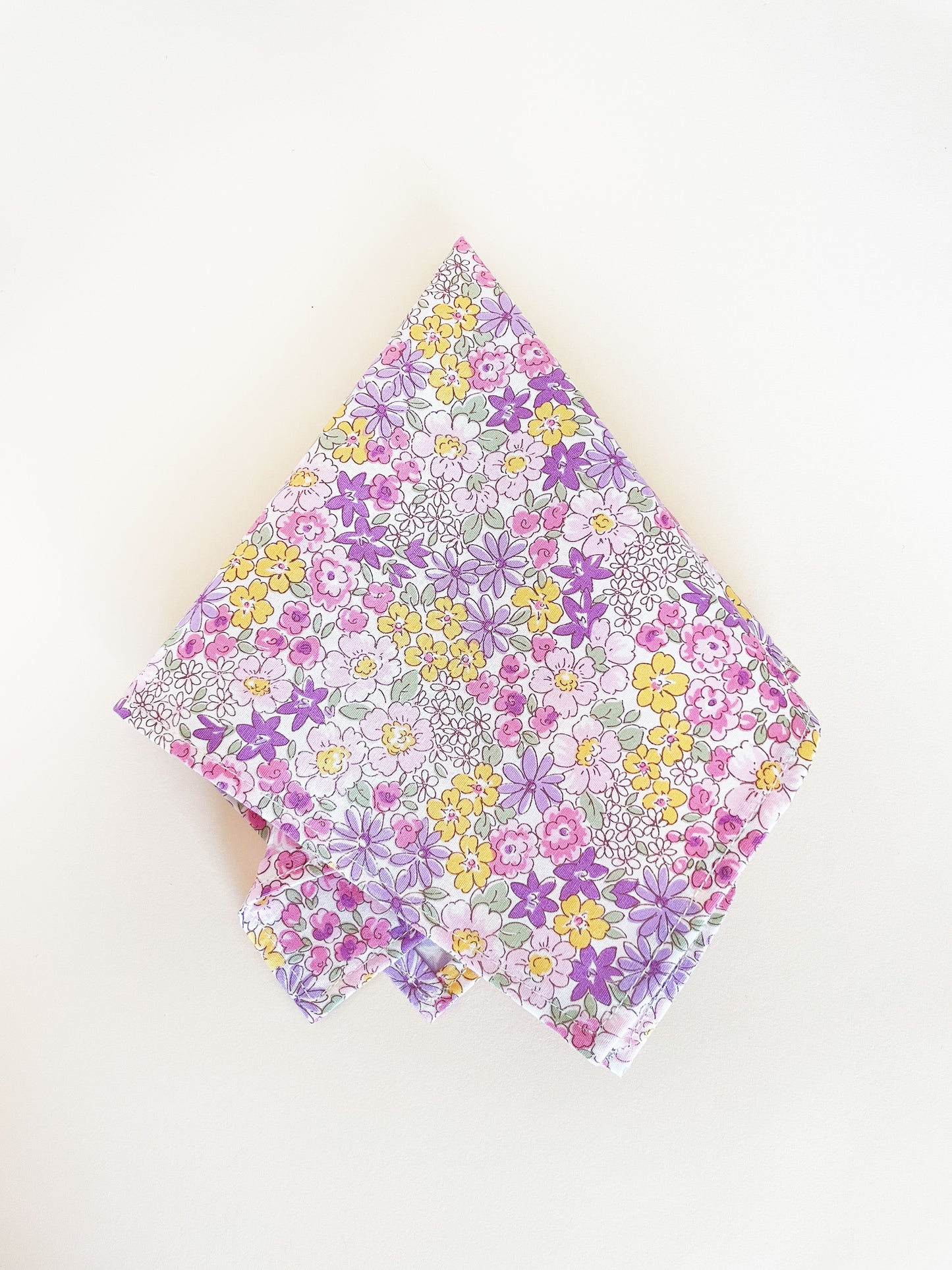 A handmade pocket square with purple flowers against an off white background.