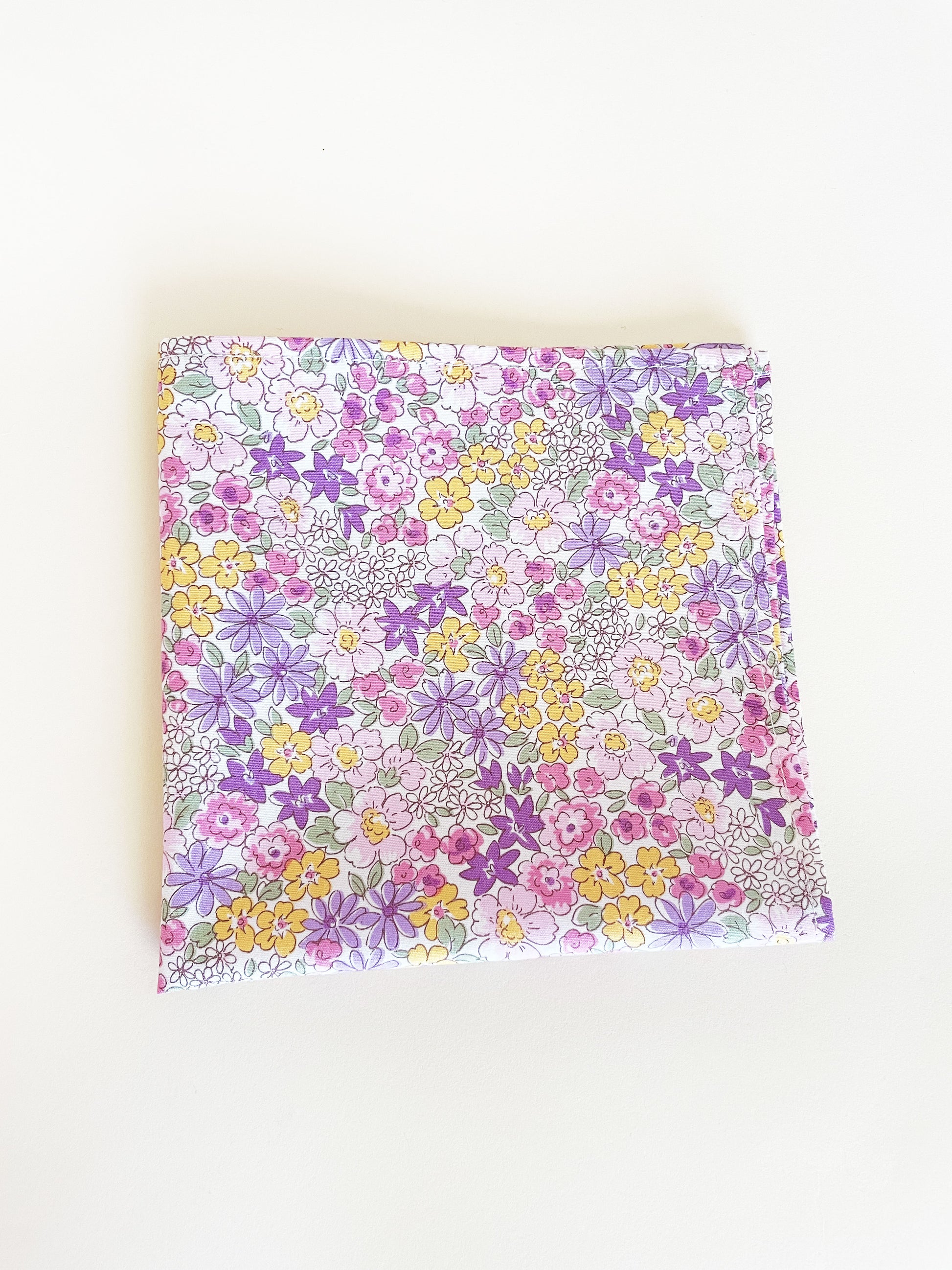 A handmade pocket square with purple flowers against an off white background.