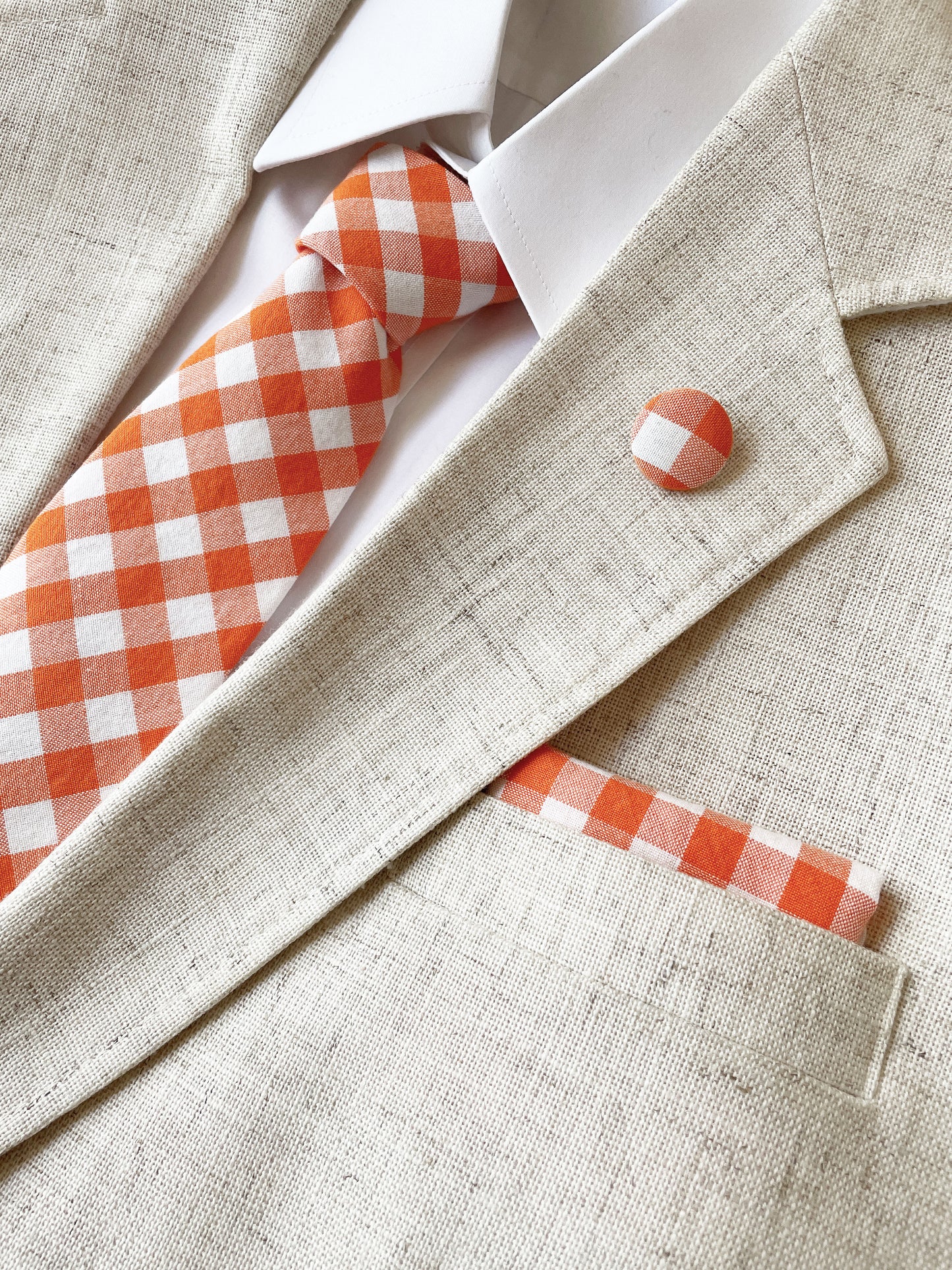 A cotton handmade pocket square with an orange gingham plaid print. The pocket square is shown with a matching necktie (sold separately).