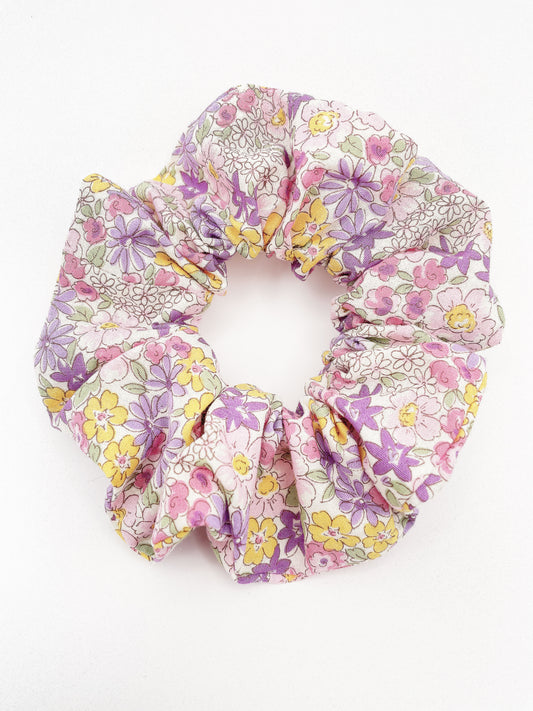 A handmade purple floral scrunchie against an off white background.