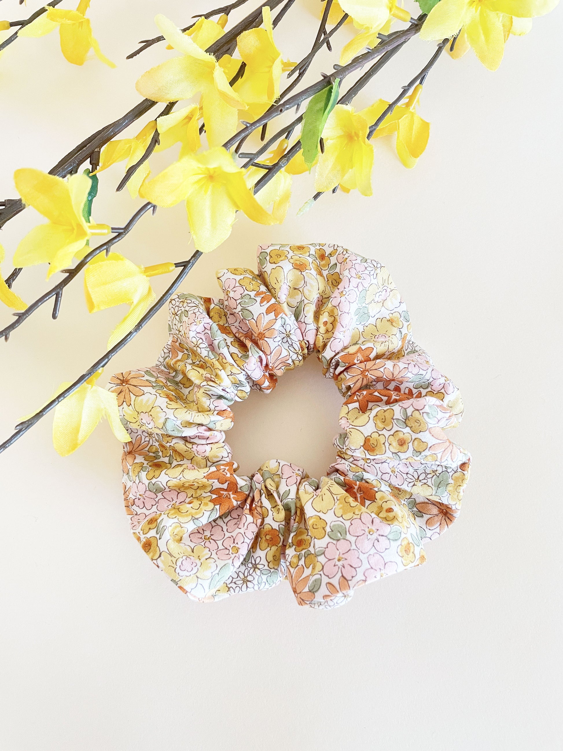 A handmade boho yellow floral scrunchie against an off white background.