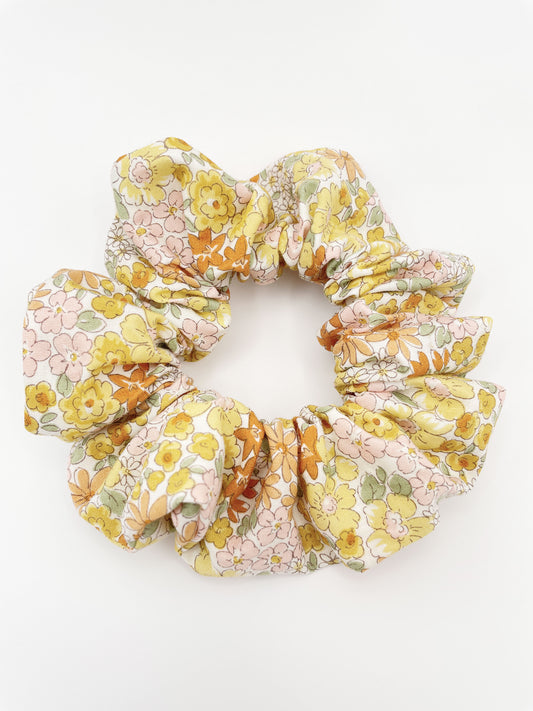 A handmade boho yellow floral scrunchie against an off white background.